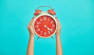 person holding red and beige twin bell analog alarm clock