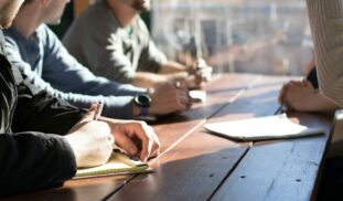 people sitting on chair in front of table while holding pens during daytime