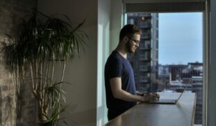 man standing beside table using laptop
