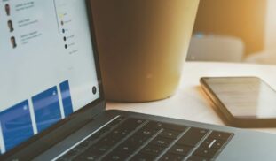 white laptop computer turned on beside brown paper cup